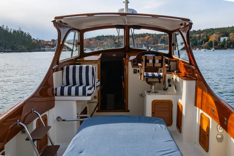 Slide: The Image of 2001 Hinckley Picnic Boat Classic interior with striped seating, overlooking serene waters and autumn foliage. - 21