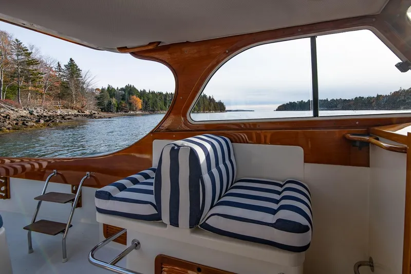 Slide: The Image of 2001 Hinckley Picnic Boat Classic interior with striped cushions, overlooking serene waters and forested shoreline. - 38