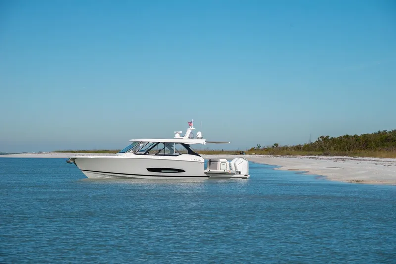 Slide: The Image of 2026 Regal LX43 boat anchored near a sandy beach under a clear blue sky. - 5