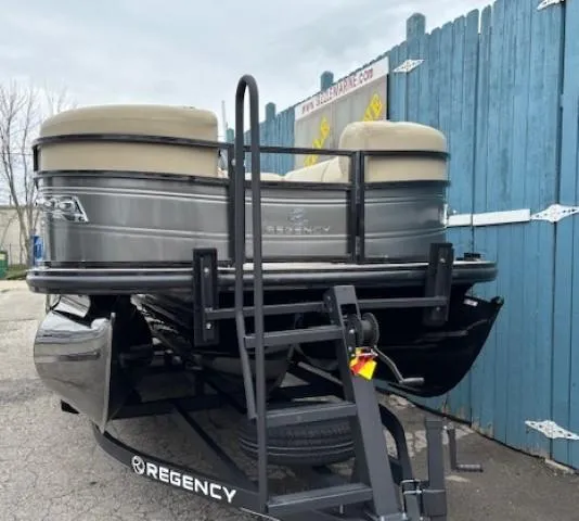 Slide: The Image of 2024 Regency 250 LE3 pontoon boat on trailer, parked by blue fence. - 2