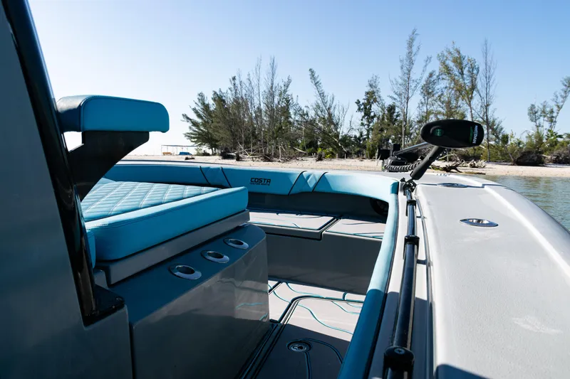 Slide: The Image of 2022 Costa Custom Boats 264 interior with blue seating, near a sandy beach. - 12