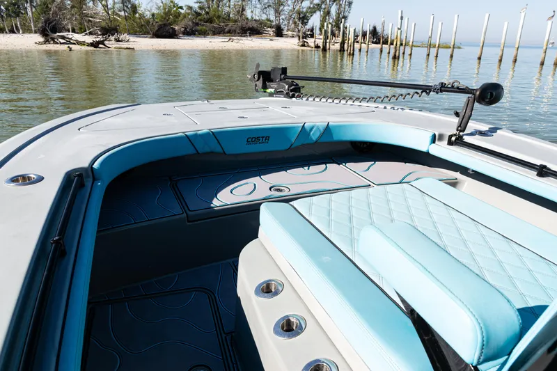 Slide: The Image of 2022 Costa Custom Boats 264 interior with blue seating, near a serene shoreline. - 14