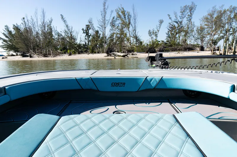 Slide: The Image of 2022 Costa Custom Boats 264 interior with turquoise seating, near a scenic shoreline. - 16