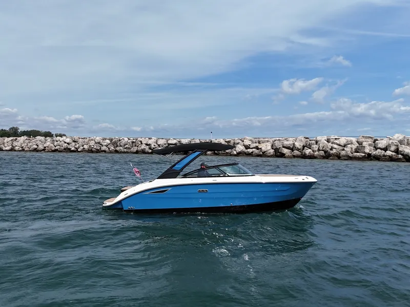 Slide: The Image of A 2026 Sea Ray SDX 250 cruising on calm waters near a rocky shoreline. - 2