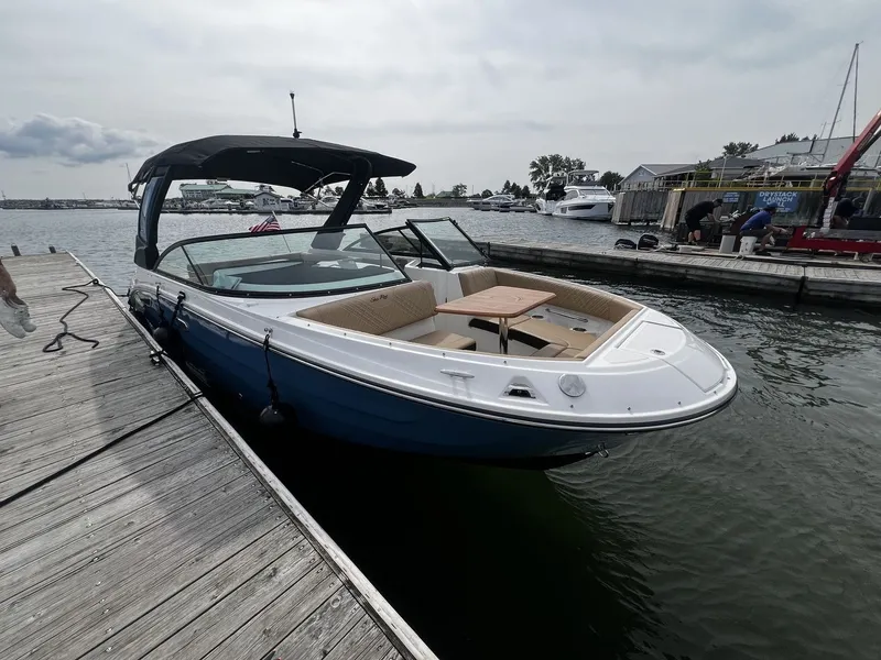 Slide: The Image of A 2026 Sea Ray SDX 250 docked. It features a blue hull design and an open deck with seating and a table. - 18