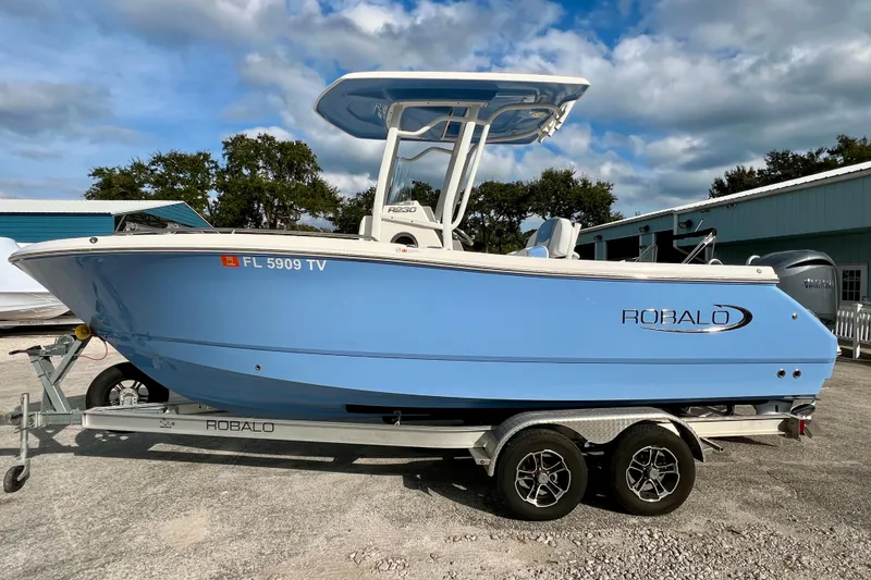 Slide: The Image of 2024 Robalo R230 Center Console boat on trailer, blue hull, parked outdoors. - 5