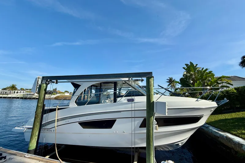 The Image of 2022 Beneteau Antares 9 docked by a scenic waterfront under a clear blue sky. - 0