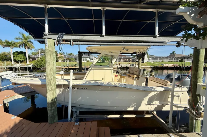 The Image of 2016 Scout 255 LXF boat docked under a canopy in a sunny marina. - 0