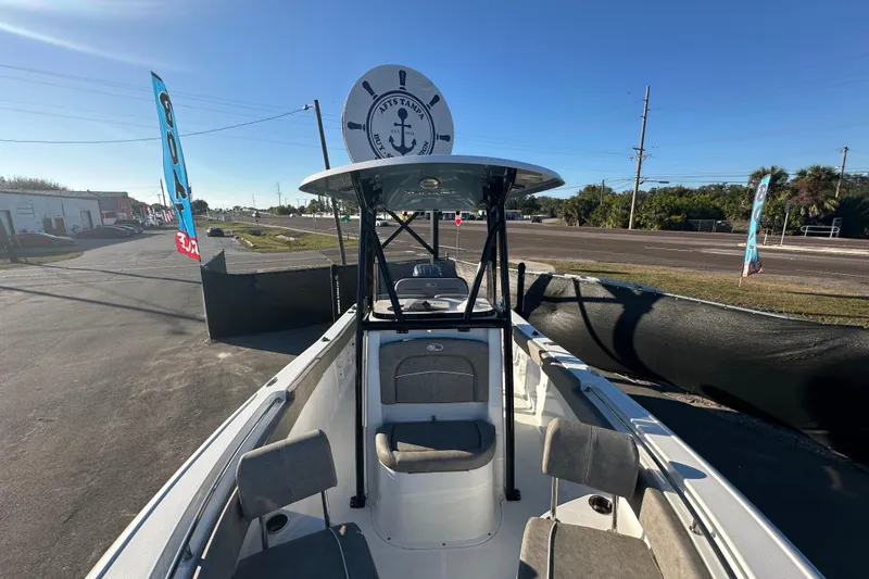 Slide: The Image of 2025 Sea Hunt Ultra 219 boat with T-top, parked outdoors under clear blue sky. - 48