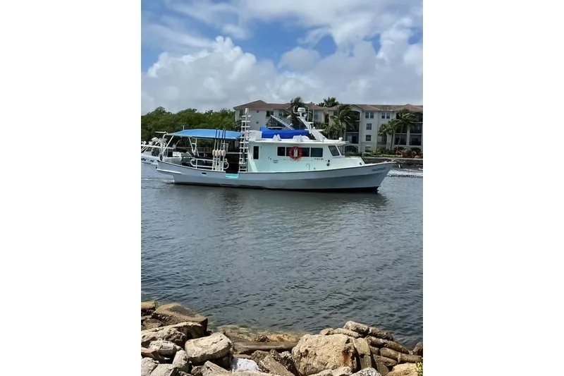 Slide: The Image of 1996 Lafitte Skiff 48 boat on calm water, with blue canopy and residential backdrop. - 6