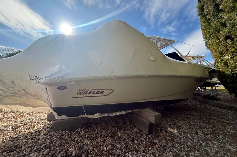 The Image of 2011 Boston Whaler 150 Super Sport boat covered, resting on wooden blocks outdoors. - 0