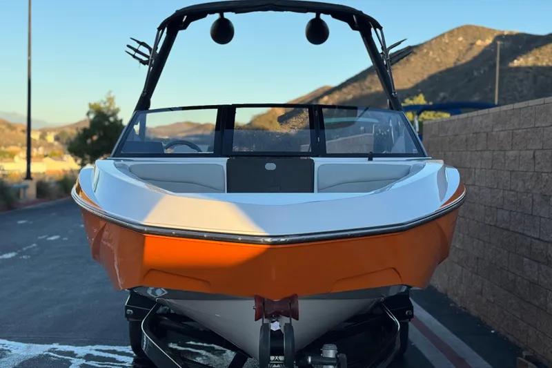 Slide: The Image of 2023 Axis T220 boat with orange hull, parked outdoors on a sunny day. - 2