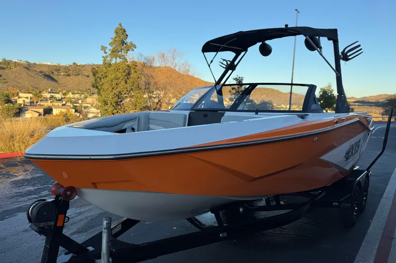 Slide: The Image of 2023 Axis T220 boat with orange and white design on a trailer, scenic background. - 3