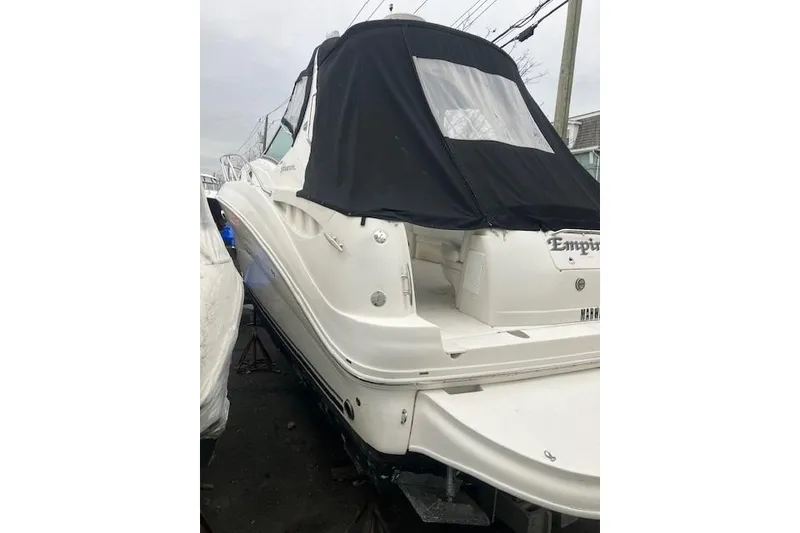 The Image of 2007 Sea Ray 320 Sundancer boat with black cover, docked outdoors. - 0