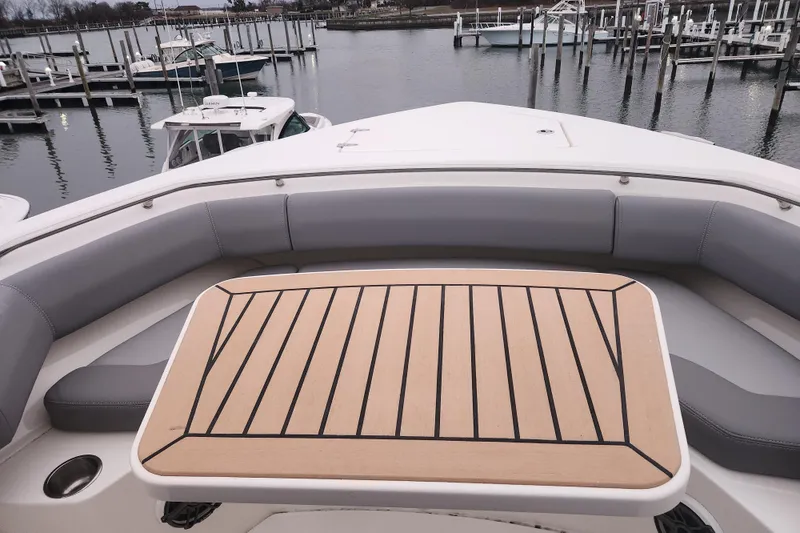 Slide: The Image of 2023 Boston Whaler 280 Outrage boat with cushioned seating and wooden table, docked at marina. - 16