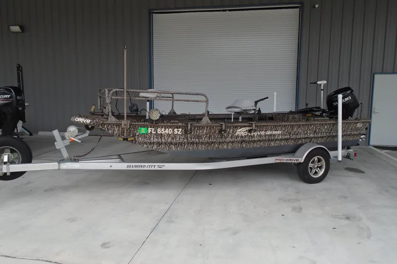 The Image of 2021 Pro-Drive SBX Series 17' boat on trailer, camo design, parked outside. - 0
