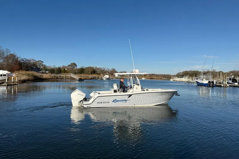 Slide: The Image of 2022 Blackfin 252 CC boat cruising on a calm river under a clear blue sky. - 1