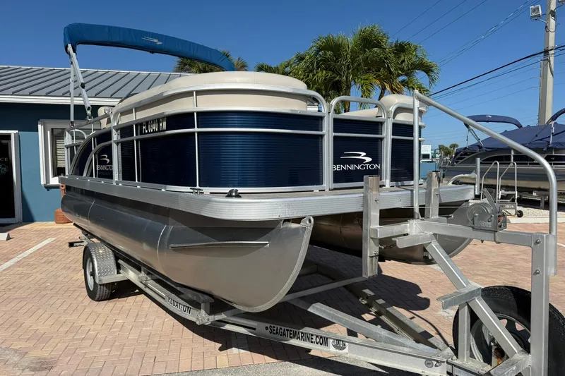 Slide: The Image of 2019 Bennington 188 SLV pontoon boat on trailer, parked outdoors under clear blue sky. - 5