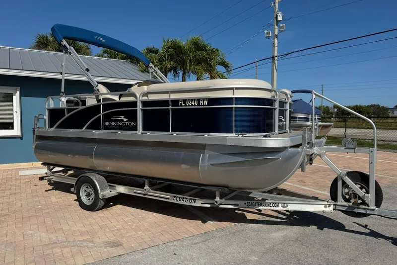 Slide: The Image of 2019 Bennington 188 SLV pontoon boat on trailer, parked near a blue building. - 6