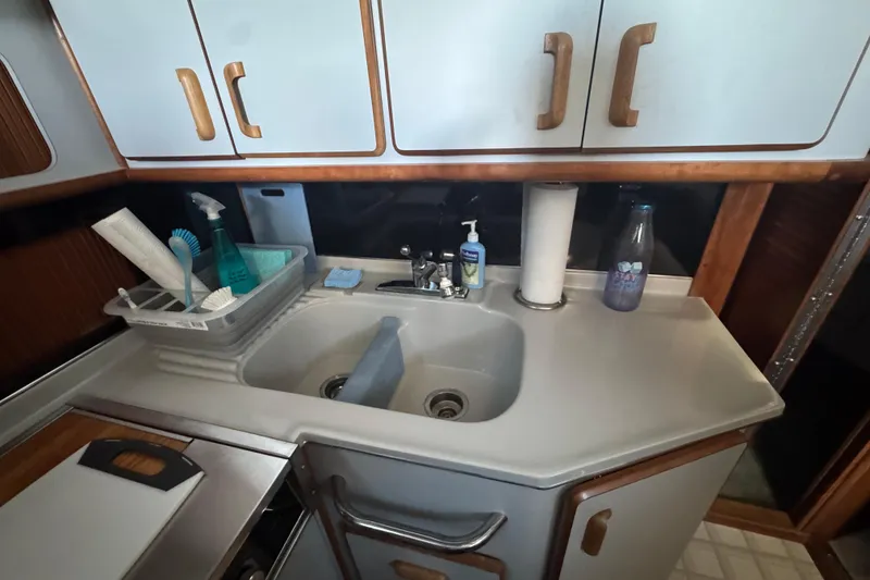 Slide: The Image of 1990 Sea Ray 380 Aft Cabin kitchen sink with cleaning supplies and cabinets. - 33