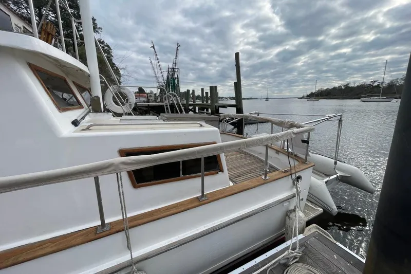 Slide: The Image of 1991 Marine Trader 34 Double Cabin docked by a serene waterfront under cloudy skies. - 60