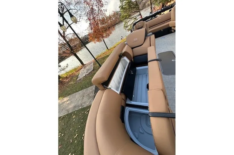 Slide: The Image of 2025 Regency 230 LE3 Sport boat interior with tan seating and storage compartments by a lake. - 11