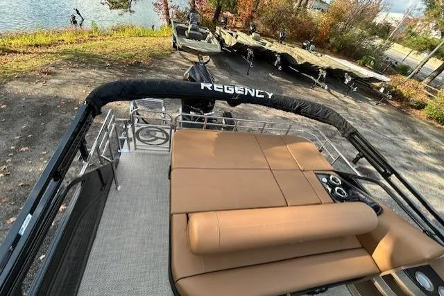 Slide: The Image of 2025 Regency 230 LE3 Sport boat with tan seating, docked near a scenic lake. - 16