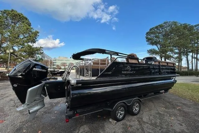 Slide: The Image of 2025 Regency 230 LE3 Sport pontoon boat on trailer, parked outdoors under blue sky. - 3