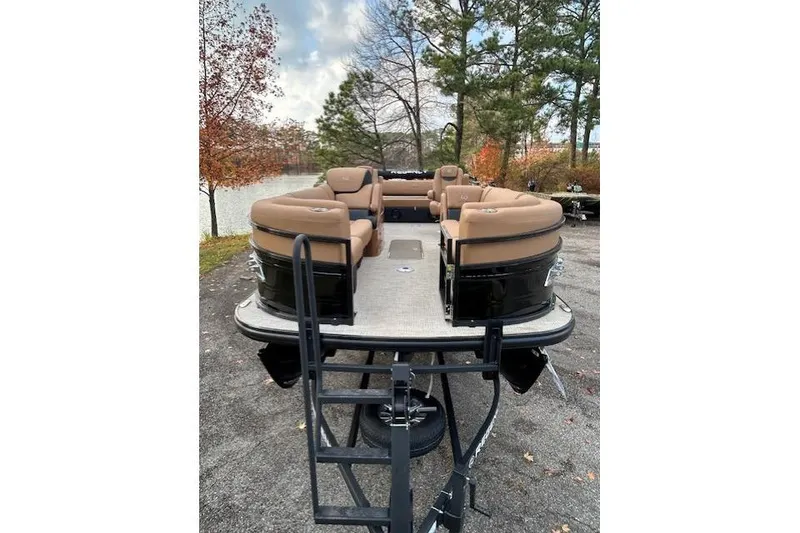 Slide: The Image of 2025 Regency 230 LE3 Sport pontoon boat with tan seating, parked near a lake. - 5