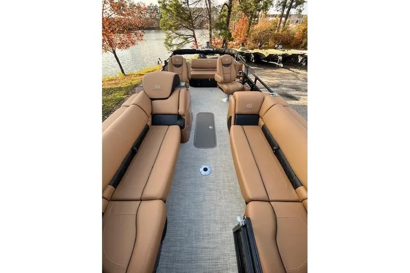 Slide: The Image of 2025 Regency 230 LE3 Sport boat interior with tan seating, lake view, and autumn trees. - 6
