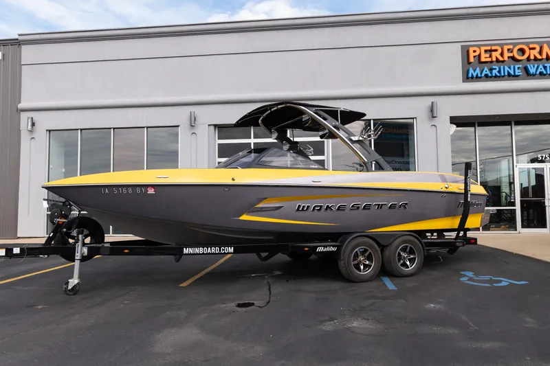 Slide: The Image of 2014 Malibu Wakesetter 24 MXZ boat in yellow and gray, parked outside a marine dealership. - 26