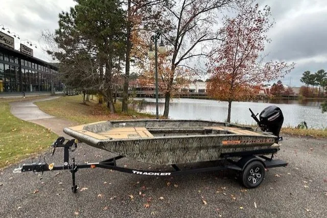 The Image of 2026 Tracker Grizzly 1756 T Marsh boat on trailer by a lake in autumn setting. - 0