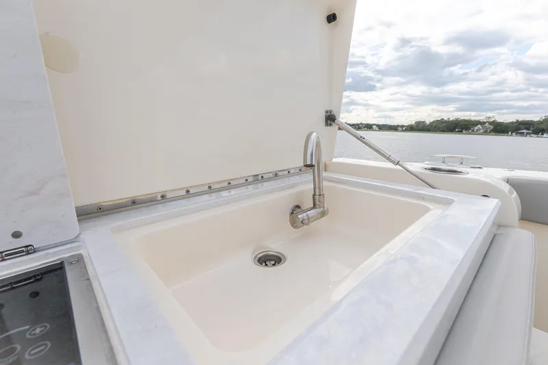 Slide: The Image of 2024 Scout 377 LXF boat sink with faucet, open lid, and scenic water view. - 19