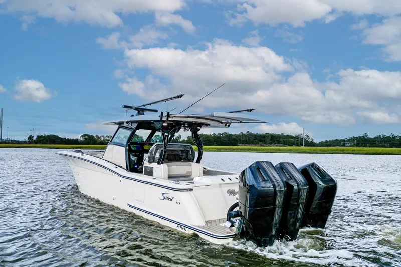 Slide: The Image of 2024 Scout 377 LXF boat cruising on a calm waterway under a partly cloudy sky. - 2