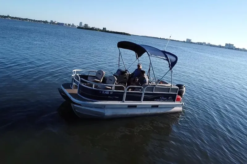 Slide: The Image of 2021 Sun Tracker Bass Buggy 16 XL pontoon boat on calm water, city skyline in background. - 16