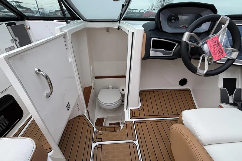 Slide: The Image of 2022 MasterCraft X26 boat interior with helm and compact bathroom. - 22