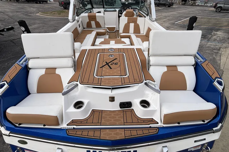 Slide: The Image of 2022 MasterCraft X26 boat interior with white and tan seating, docked in a parking area. - 48