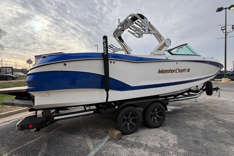 Slide: The Image of 2022 MasterCraft X26 boat on trailer, blue and white design, parked outdoors. - 57