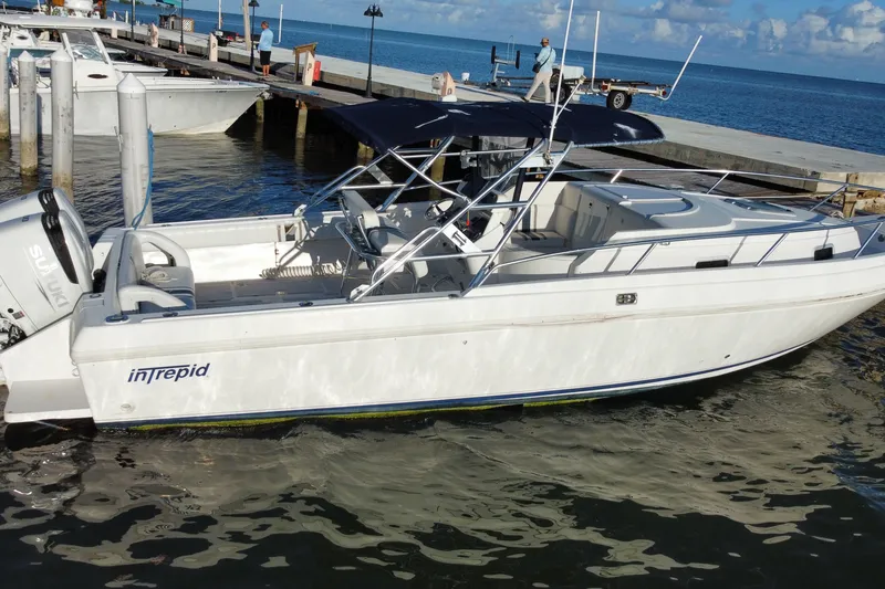 Slide: The Image of 1998 Intrepid 339 boat docked by the ocean, featuring a Suzuki outboard motor. - 14