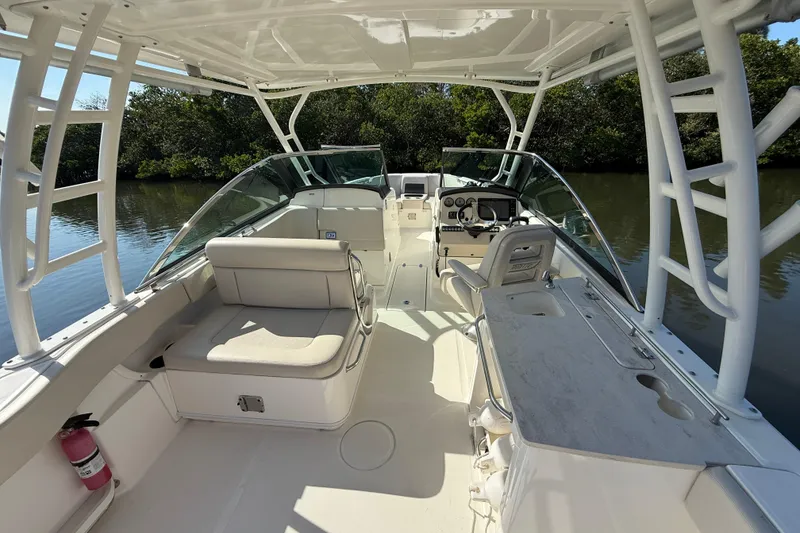 Slide: The Image of 2018 Boston Whaler 270 Vantage boat interior with seating and helm, docked by lush greenery. - 12