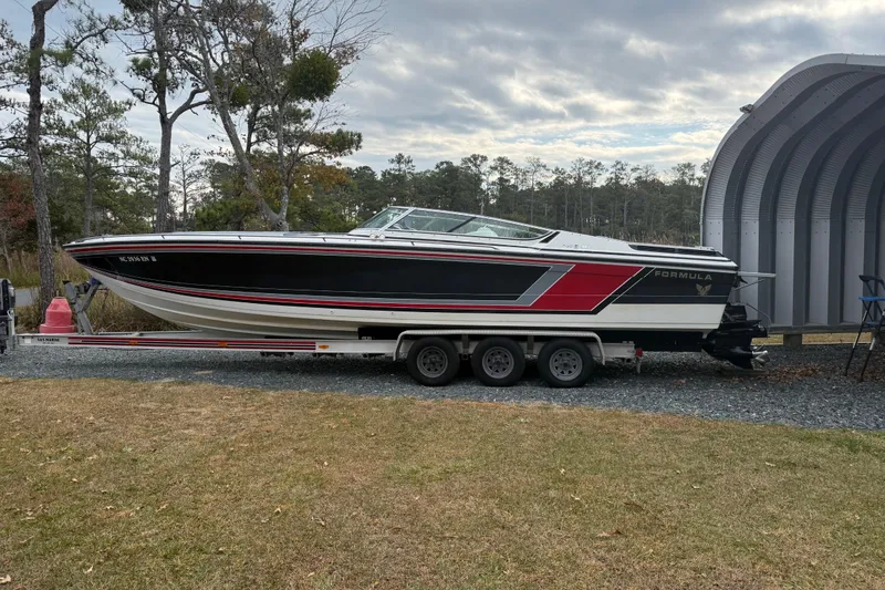 Slide: The Image of 1988 Thunderbird Formula 311 SR1 boat on trailer, parked outdoors near trees and a metal structure. - 3