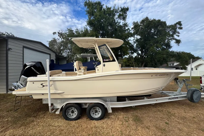 The Image of 2023 Scout 240 XSF boat on trailer, parked outdoors near trees and buildings. - 0