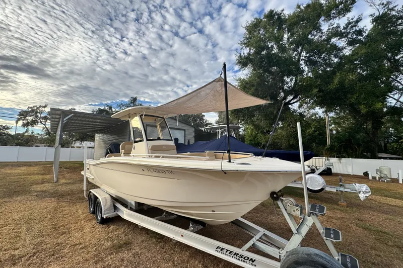 Slide: The Image of 2023 Scout 240 XSF boat on trailer under cloudy sky, parked on grass. - 2