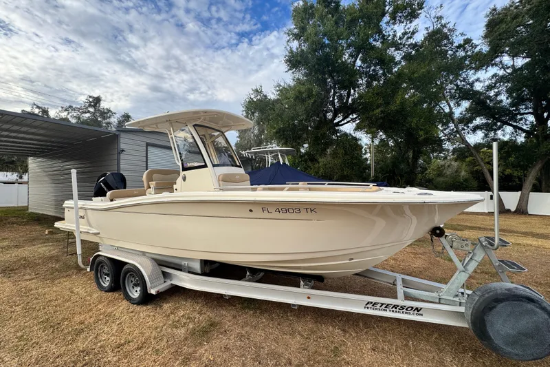 Slide: The Image of 2023 Scout 240 XSF boat on trailer, parked outdoors with trees in background. - 3