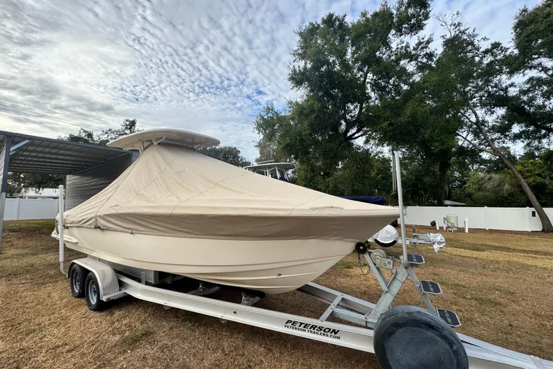 Slide: The Image of 2023 Scout 240 XSF boat covered on trailer, parked outdoors under cloudy sky. - 37