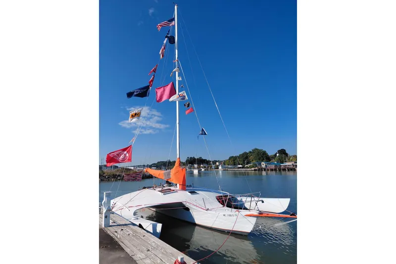 The Image of Sailboat "Newick Native" 1979 model with colorful flags docked by a serene waterfront. - 0