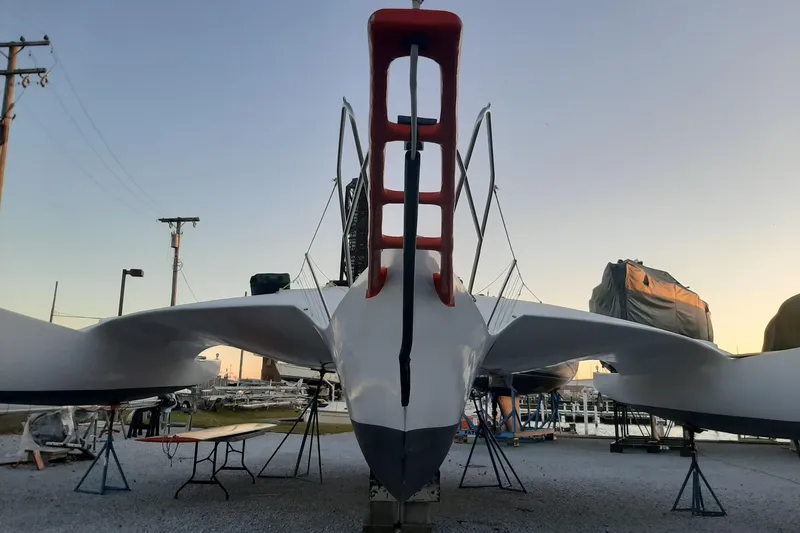 Slide: The Image of Front view of a 1979 Newick Native trimaran sailboat on land at sunset. - 3