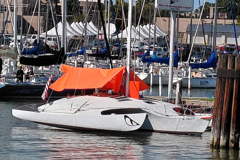 Slide: The Image of Sailboat in marina, Newick Native 1979, with orange canopy and American flag. - 6