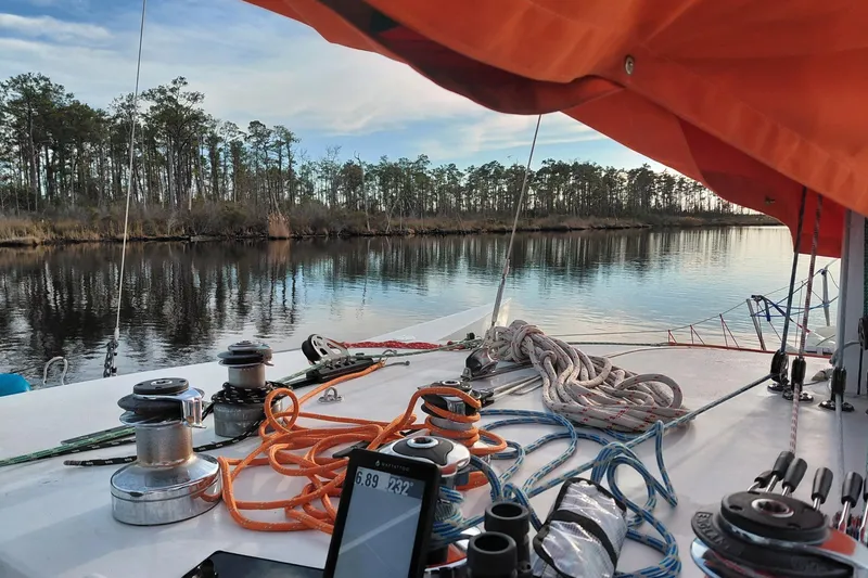 Slide: The Image of Sailboat deck with ropes and winches, Newick Native 1979, serene river view. - 7