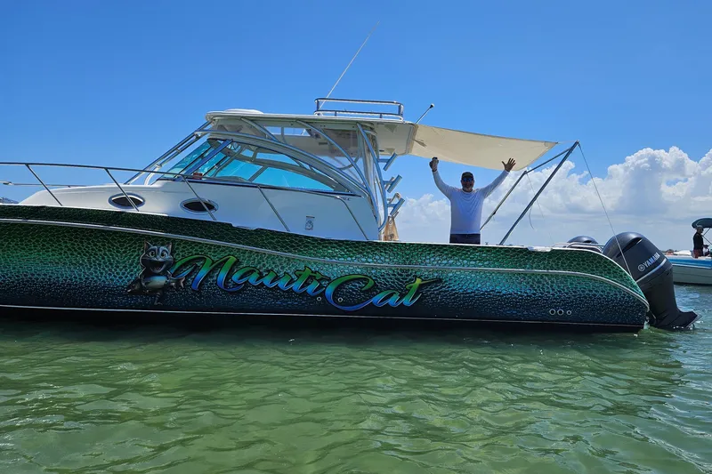 Slide: The Image of 2014 World Cat 320 EC boat on water with person waving, clear sky background. - 2